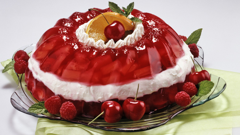 A 1950's style Jell-O mold with a cream layer decorated with raspberries, cherries, mint, and an orange slice.