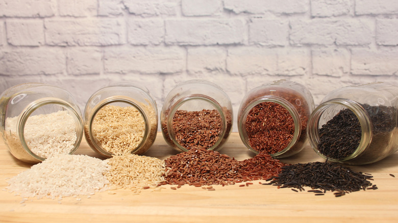 Various types of rice in glass jars spilling onto a counter