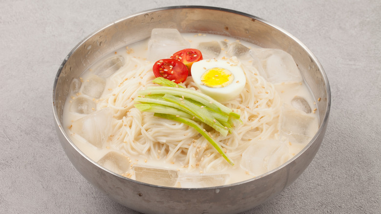 metal bowl of noodle soup with ice cubes