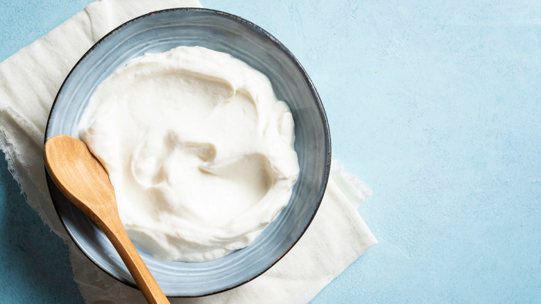 Plain greek yogurt in a grey bowl with a wooden spoon on a pale blue background