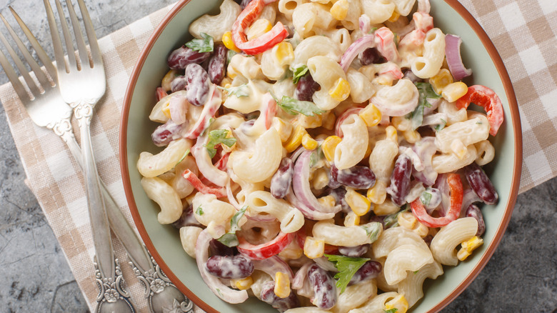 Pasta salad with onions and corn in a pale green bowl with a brown rim