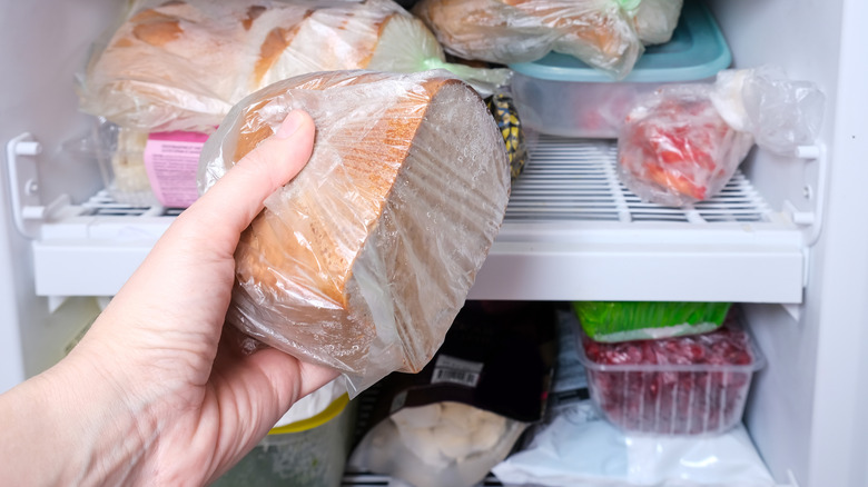 A person placing a loaf of bread in a freezer.