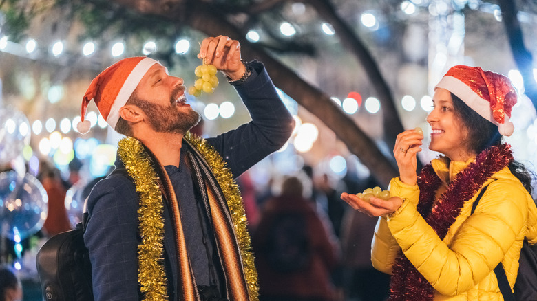 Two people with Santa hats eat grapes off a vine