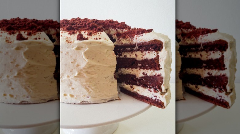 A slice of chocolate layer cake with a creamy white icing is being removed from the whole cake