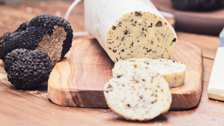 Roll of truffle butter on board next to fresh black truffles