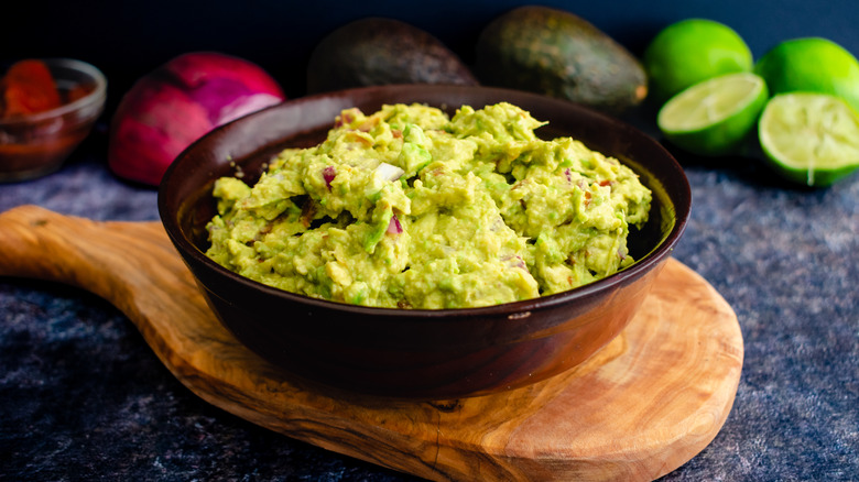 Homemade guacamole in a bowl with cilantro, onions, limes, and avocado