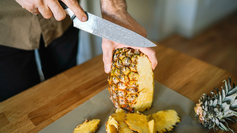 Person cutting a whole pineapple