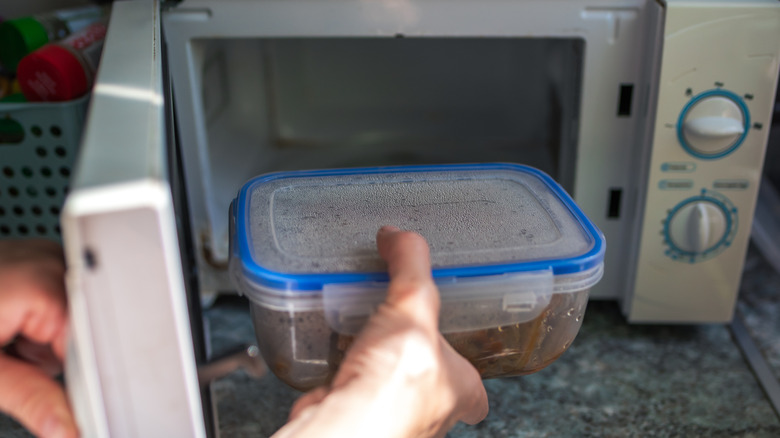 Person putting a plastic container of food into the microwave