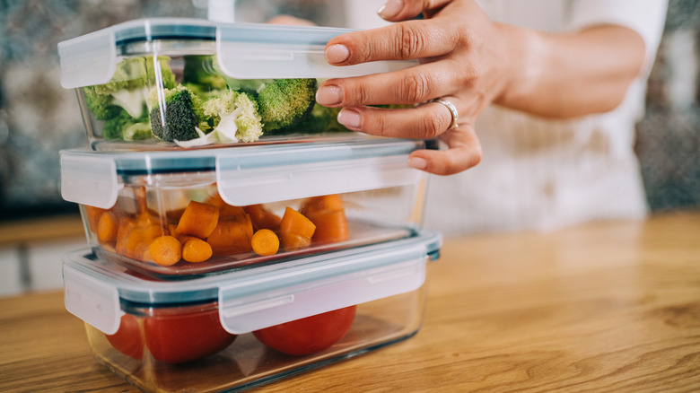 Someone stacking glass containers that are filled with raw vegetables