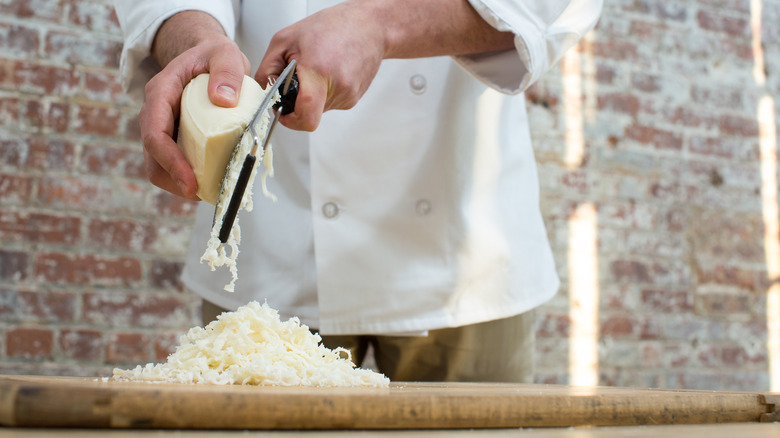 A chef shredding cheese onto a wooden cutting board