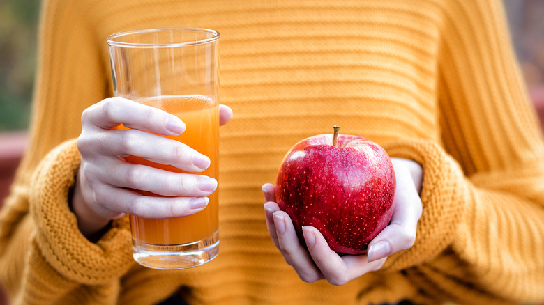 a woman in a yellow sweater holding an apple and apple cider