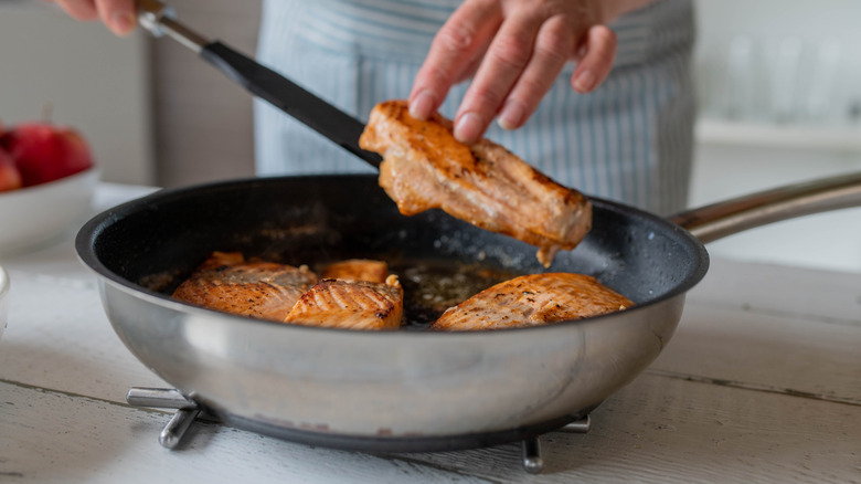 woman serving seared salmon fillets from pan