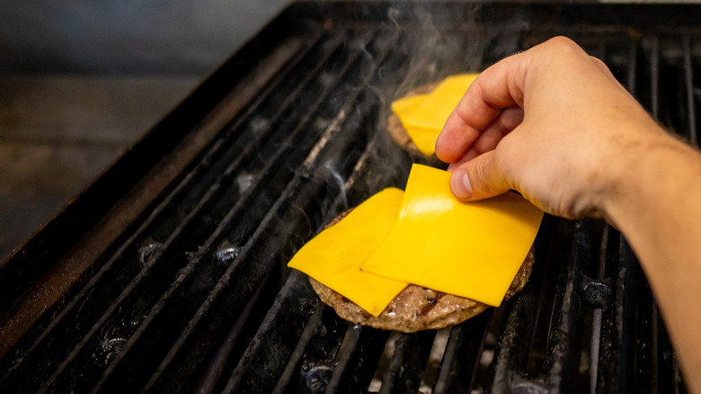 A hand placing slices of cheese on a burger patty as it cooks