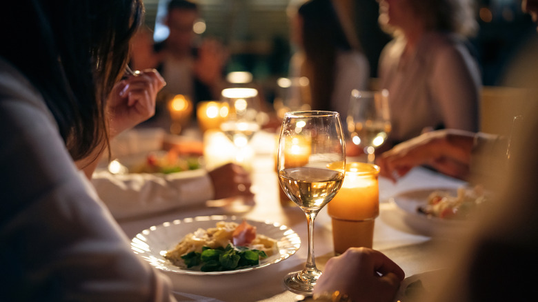 A person drinking white wine paired with a plate of pasta