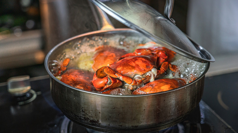 Whole crabs cooking in a silver pot with the lid half removed