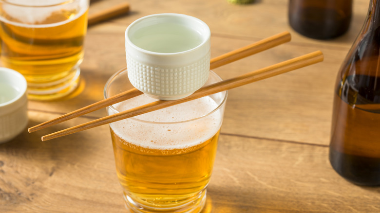 A glass of beer with a shot of sake resting on two chopsticks.