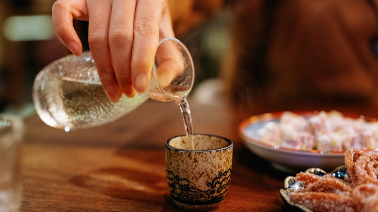 A person pouring hot sake into a small cup.