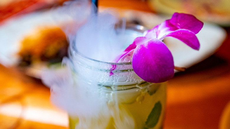 A drink in a glass jar chilled with dry ice and decorated with a flower