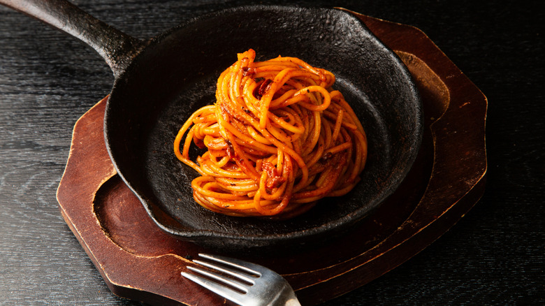 Spaghetti all'assassina in a pan on a wooden board with a fork