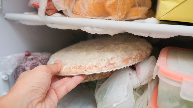 a hand pulling a frozen pizza from a freezer