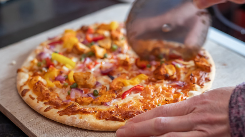 a pizza being sliced on wooden cutting board