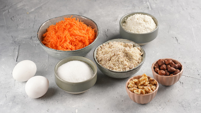 Grated carrots and other ingredients for carrot cake in bowls on a countertop