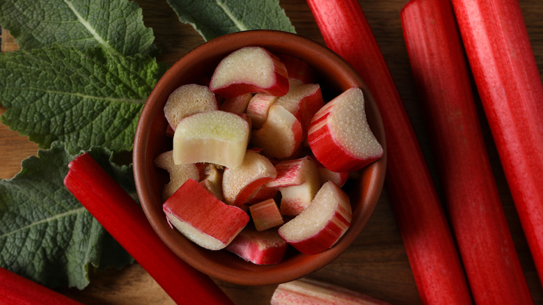 Freshly cut rhubarb in bowl with stalks and leaves