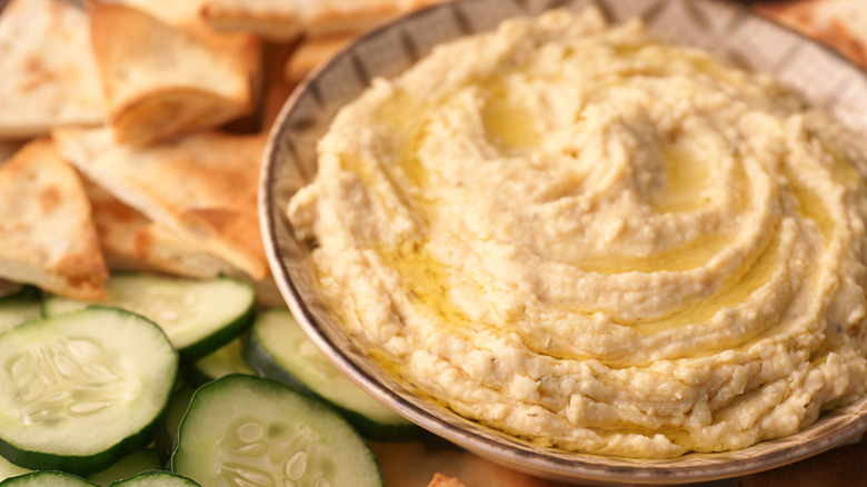 a bowl of hummus surrounded by cucumber slices and pita triangles