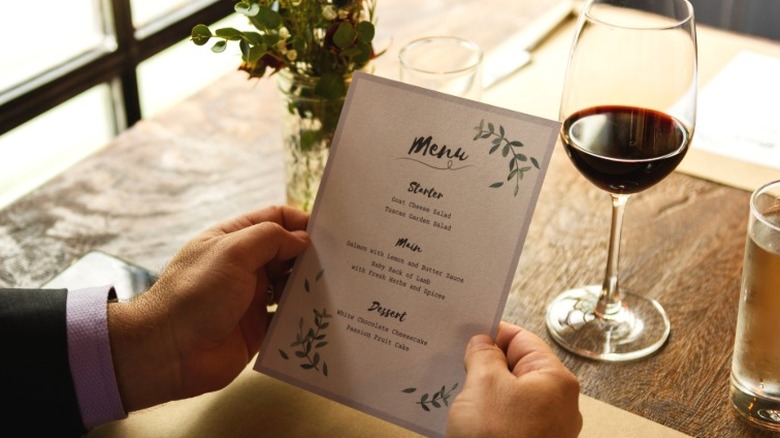 A pair of hands holding a menu at a restaurant table.