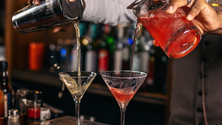 Two cocktails poured at a bar, one from a shaker, one from a glass