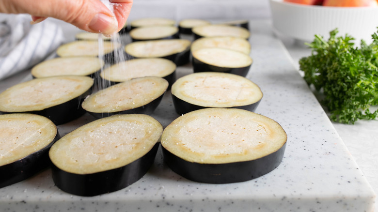 Salting eggplant slices on a chopping block