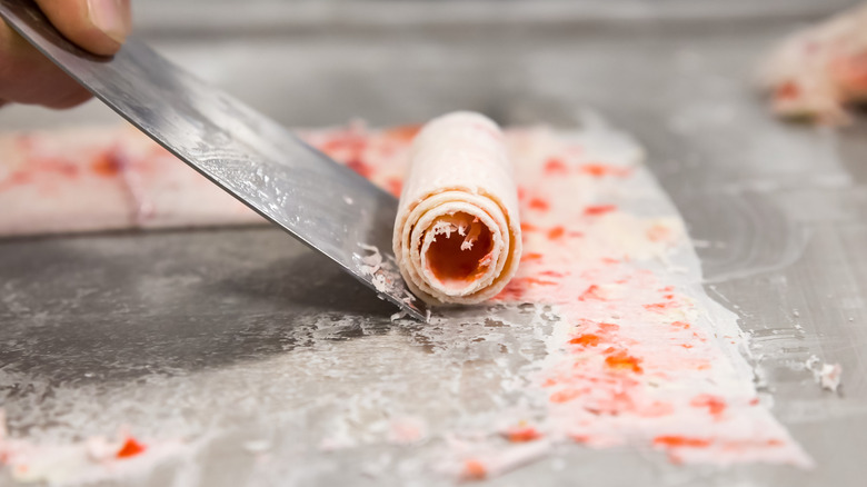 Someone scraping a roll of pink ice cream for ice cream rolls