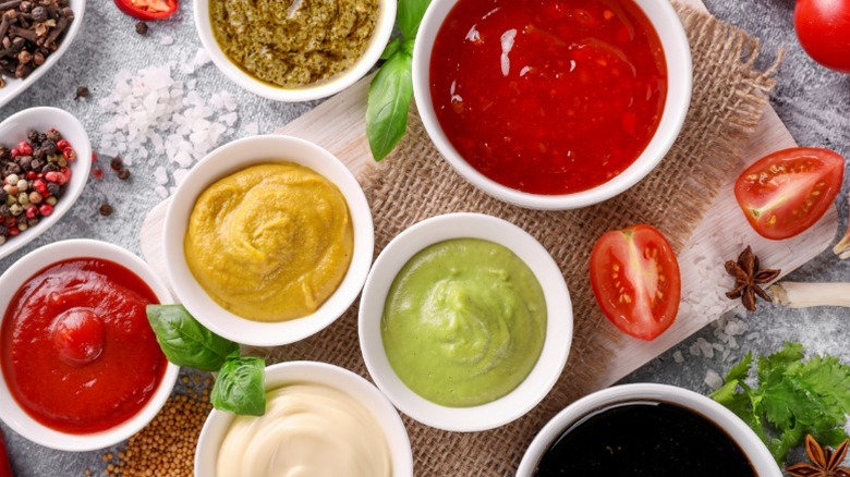 Several condiments in white bowls on a wooden board