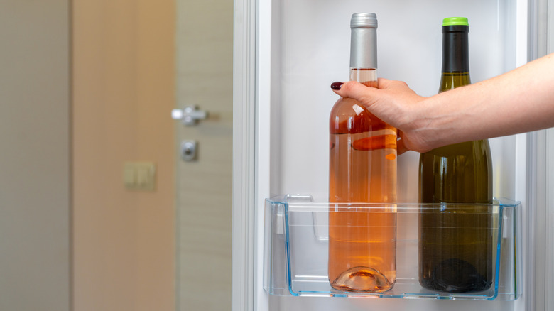 Hands reaching for bottle of wine in refrigerator door