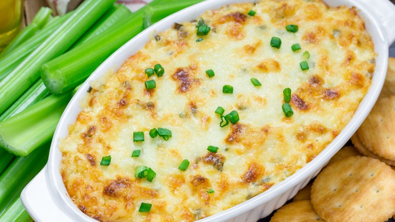 Container of crab dip surrounded by celery sticks and crackers.