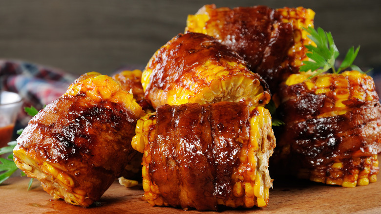 Several half-cobs of corn wrapped in bacon and covered in BBQ sauce