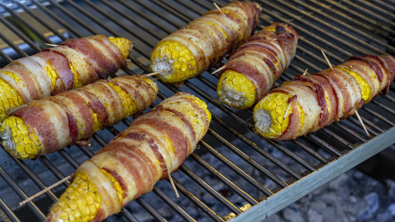 six cobs of corn wrapped in bacon laying on a grill