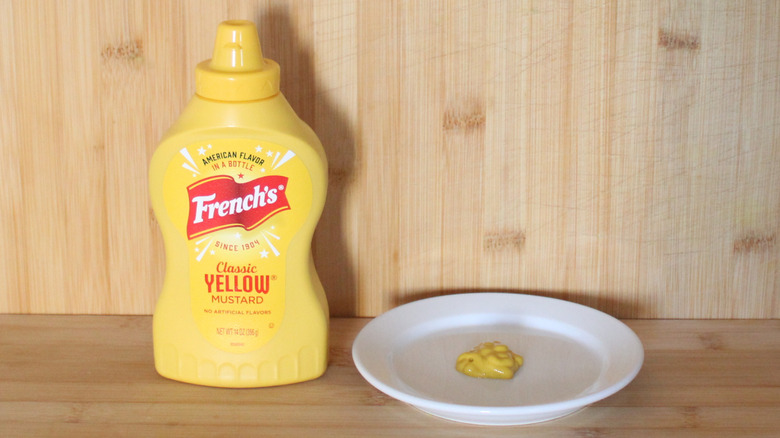 A bottle of French's yellow mustard on a wooden backdrop