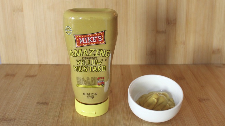 A bottle of Mike's Amazing yellow mustard on a wooden background