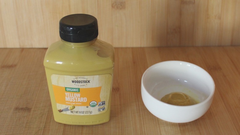 A bottle of Woodstock organic yellow mustard on a wood background