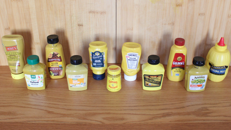 An array of mustard bottles in front of a neutral wood background