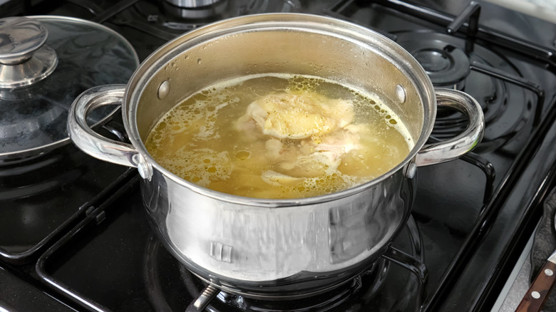 Chicken boiling in water inside a metal pot on top of a stove.