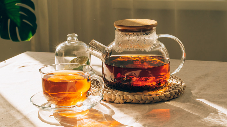 A tea pot with tea inside beside a teacup full of tea