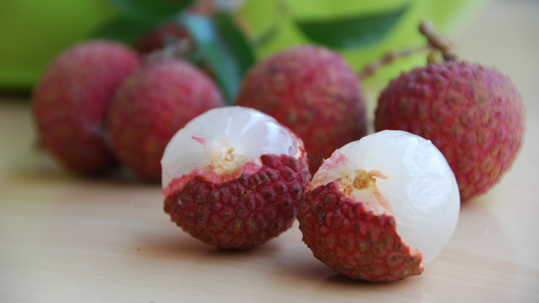 Lychees with rough red skin, with two lychees half-peeled showing the glassy white flesh underneath,