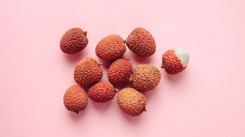 Several fresh lychees on a pink background, one of them half-peeled.