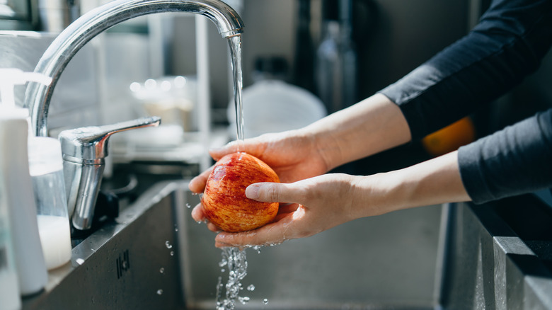 Washing a red apple under a running faucet