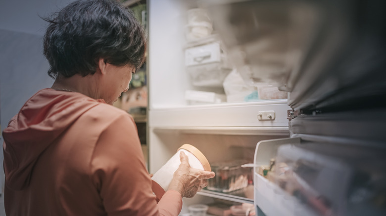 Woman holding ice cream in front of freezer