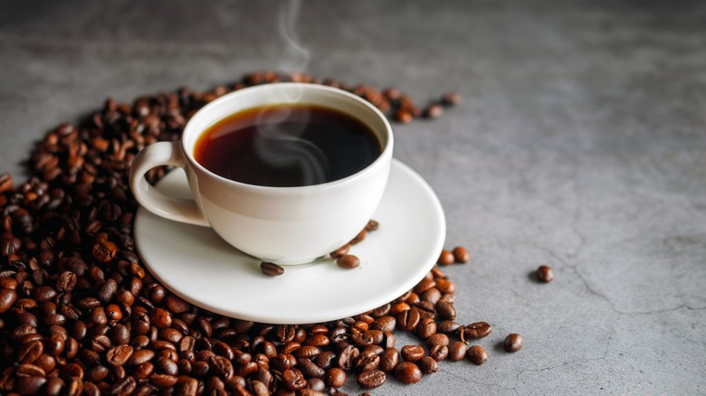 A hot cup of coffee surrounded by coffee beans