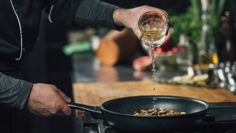 Person adding cup of white wine to mushroom dish in a pan