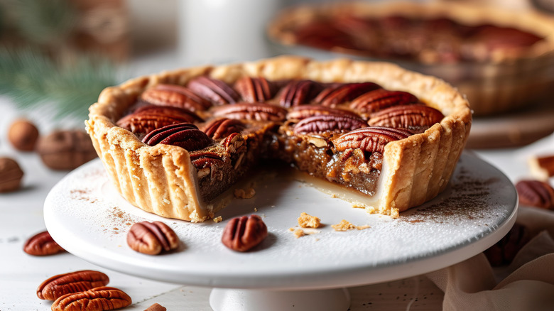 A whole pecan pie on a cake stand with a slice missing